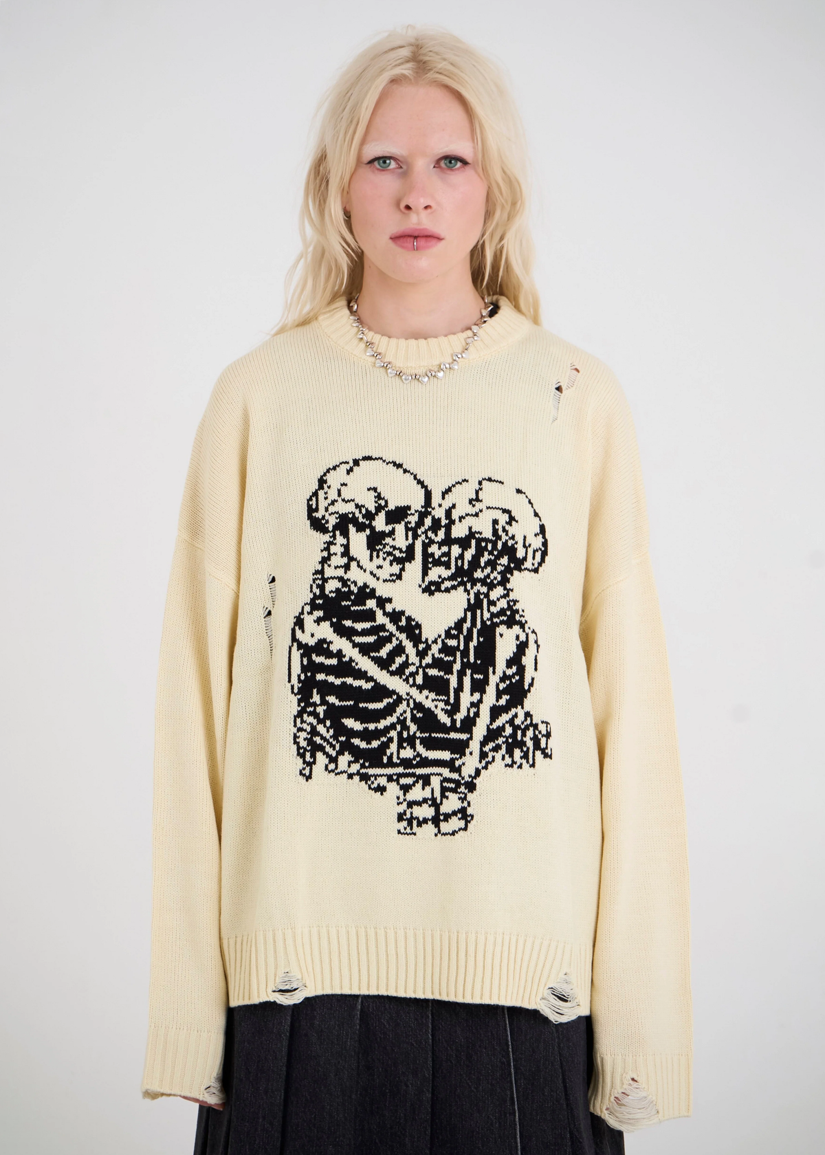 Person wearing a cream sweater with a black skeleton design on a plain background