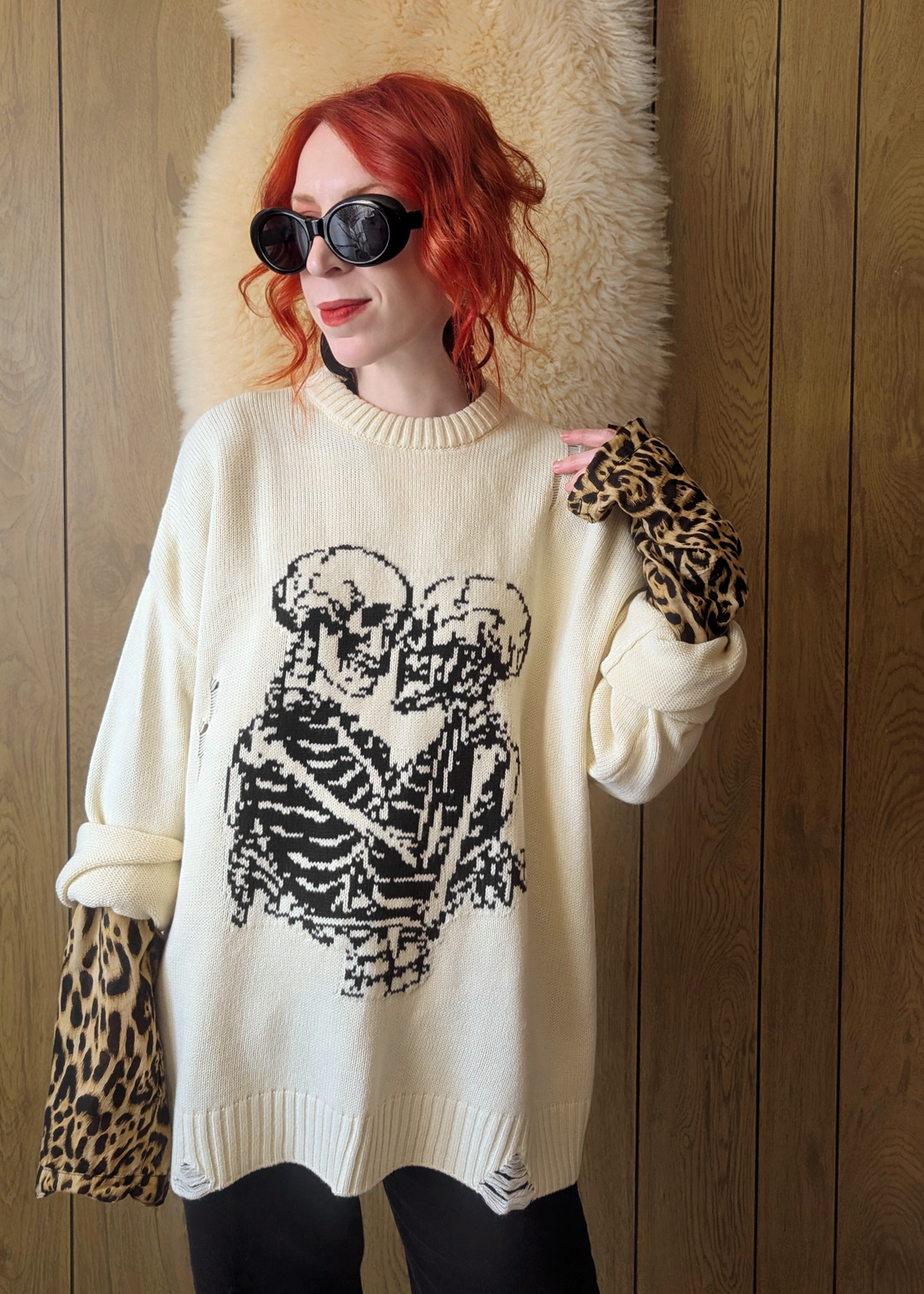 Person wearing a cream sweater with a skeleton design, standing against a wooden wall.