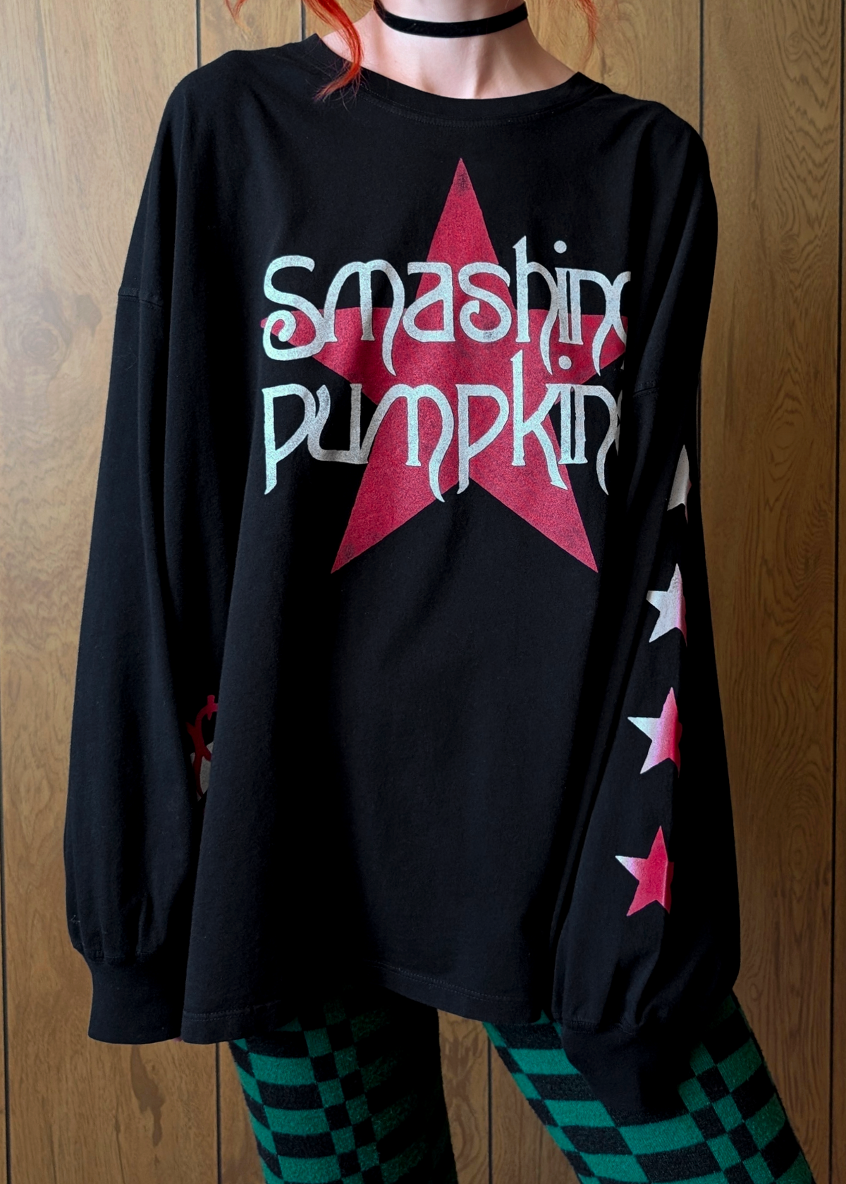Black long-sleeve shirt with 'Smashing Pumpkin' design worn by a person against a wooden background