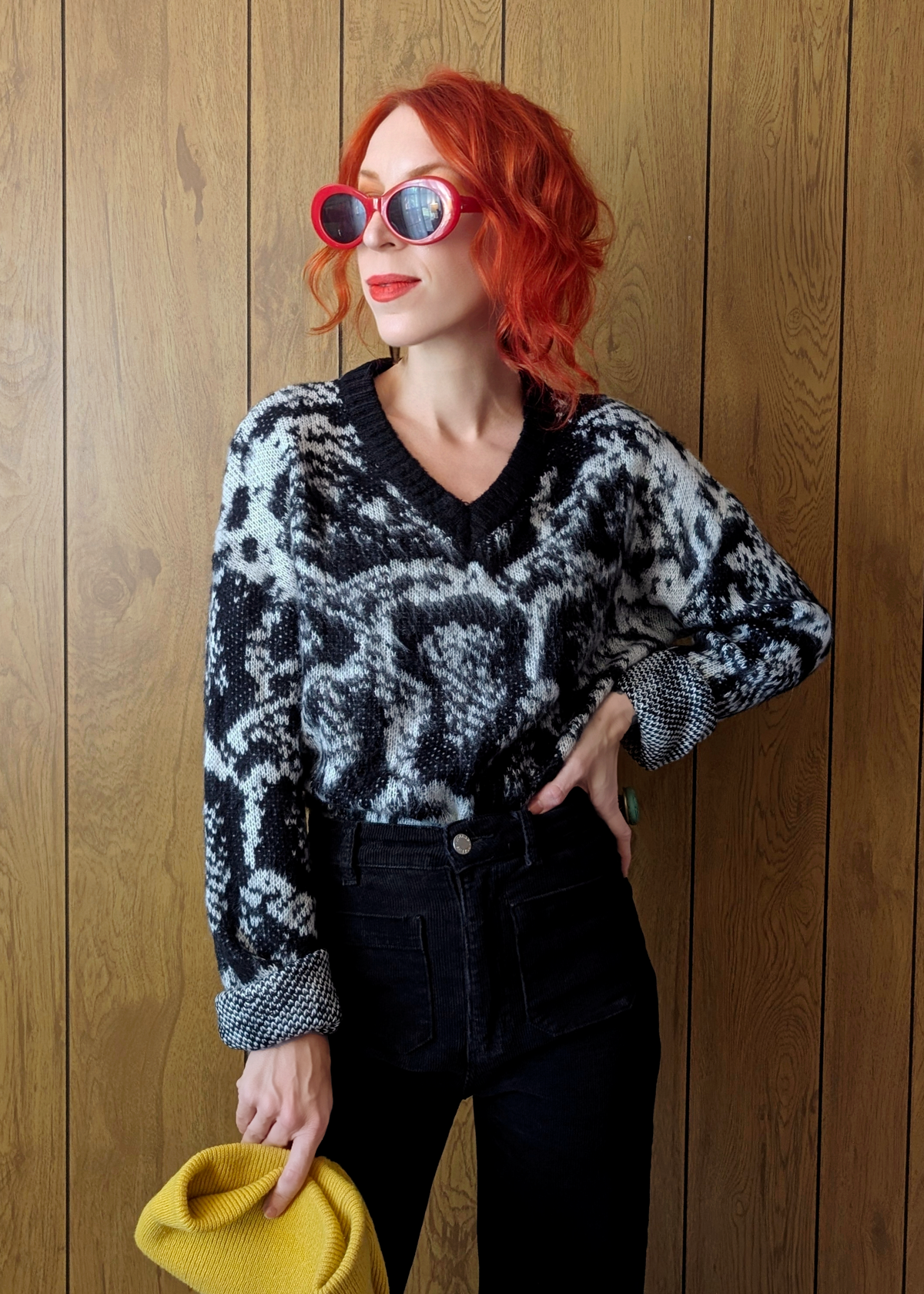 Person wearing a patterned sweater and sunglasses against a wooden background