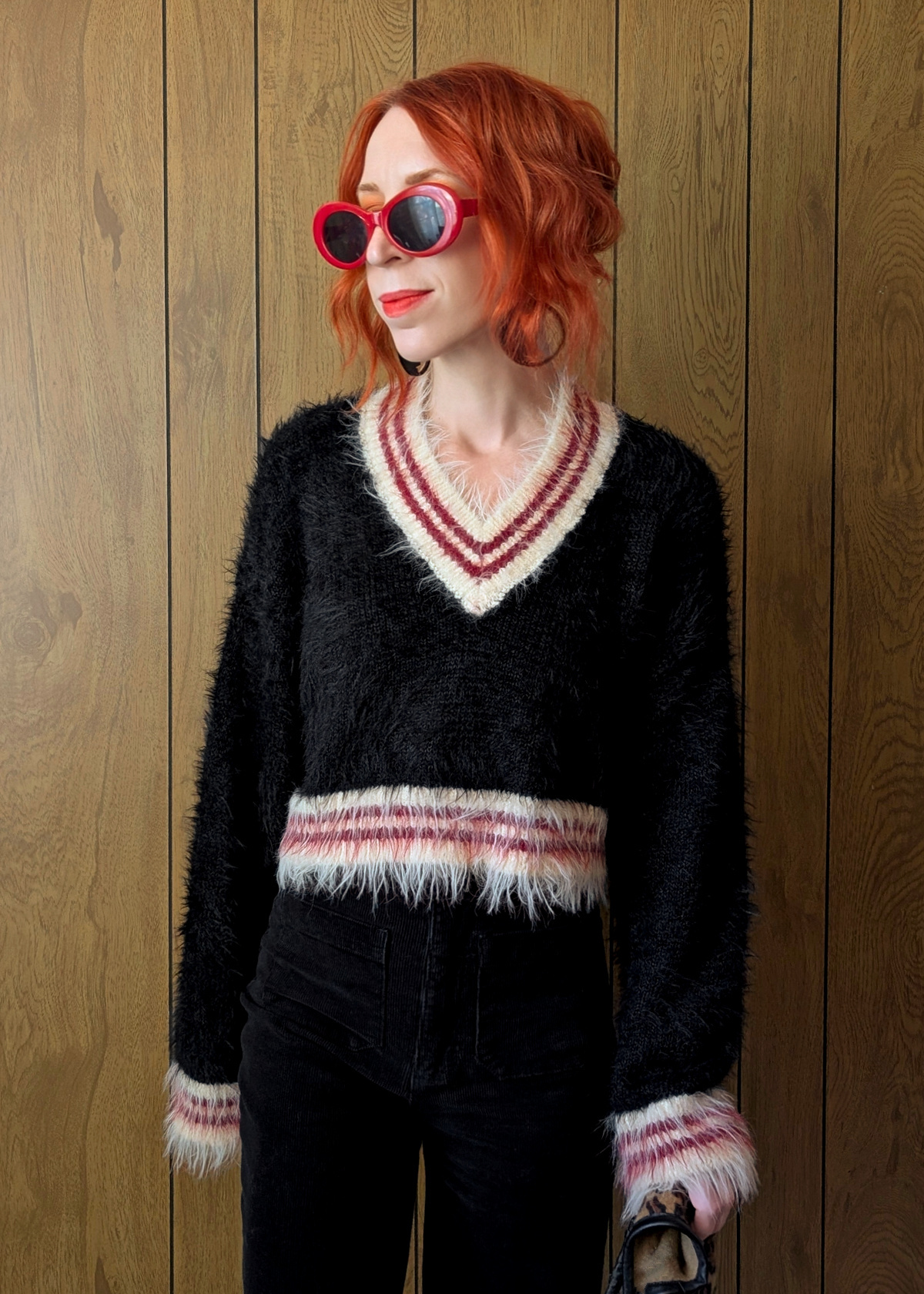Person wearing a black sweater with cream and red pattern, standing against a wooden wall.