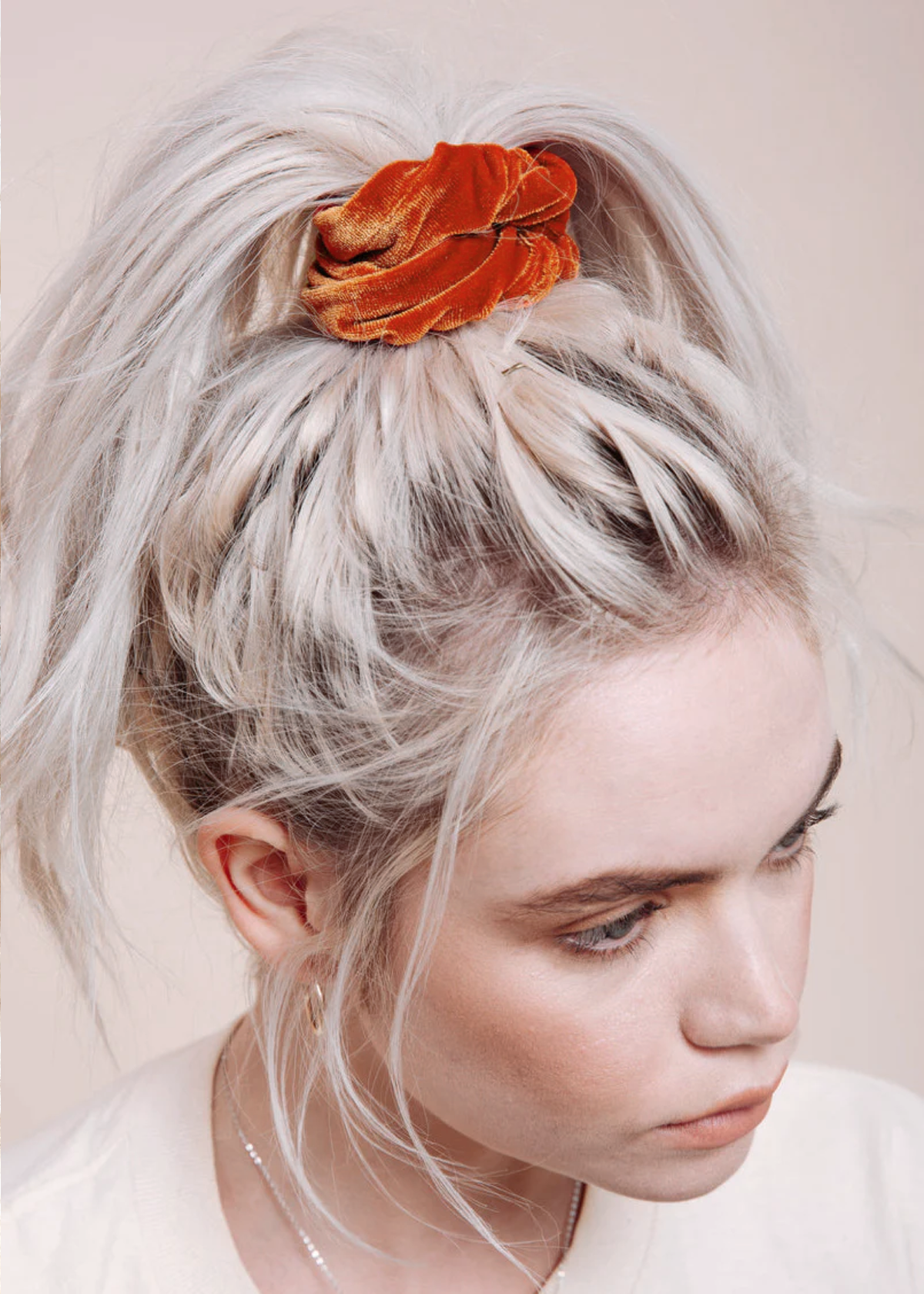 Woman with blonde hair styled in a high ponytail with an orange scrunchie against a neutral background