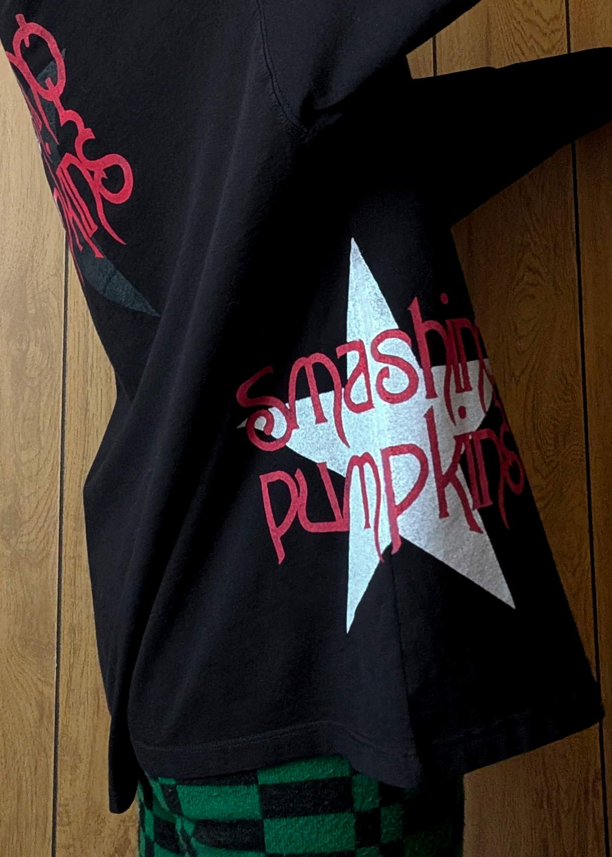 Black shirt with 'Smashing Pumpkins' logo  worn against a wooden backdrop 