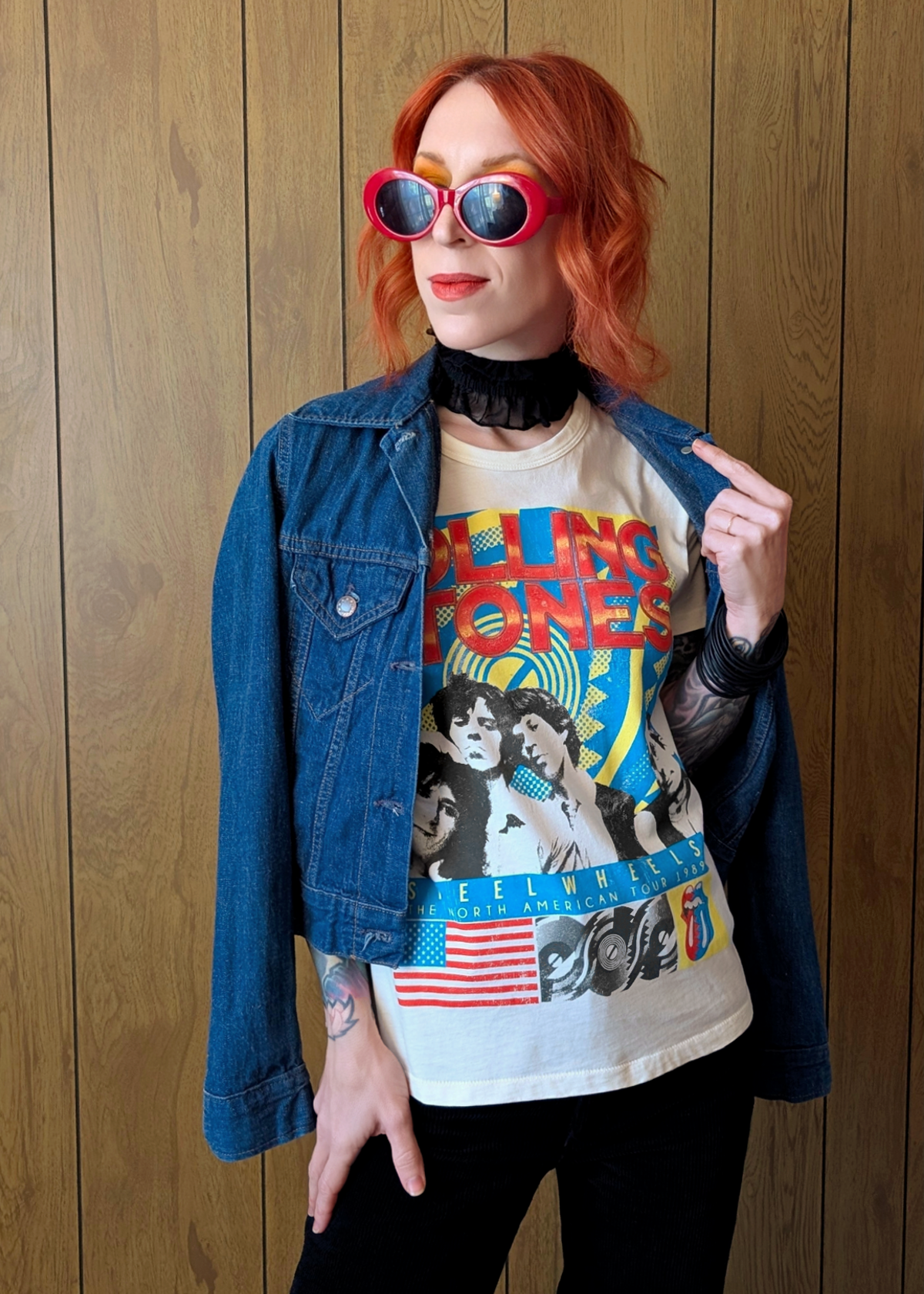 Person wearing a Rolling Stones graphic t-shirt with colorful design and denim jacket against a wooden background