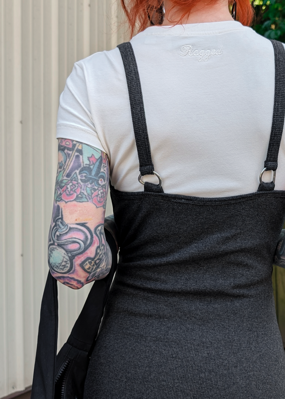 Back view of a woman wearing a white shirt layered under a ribbed charcoal slip dress with D-ring details on straps.