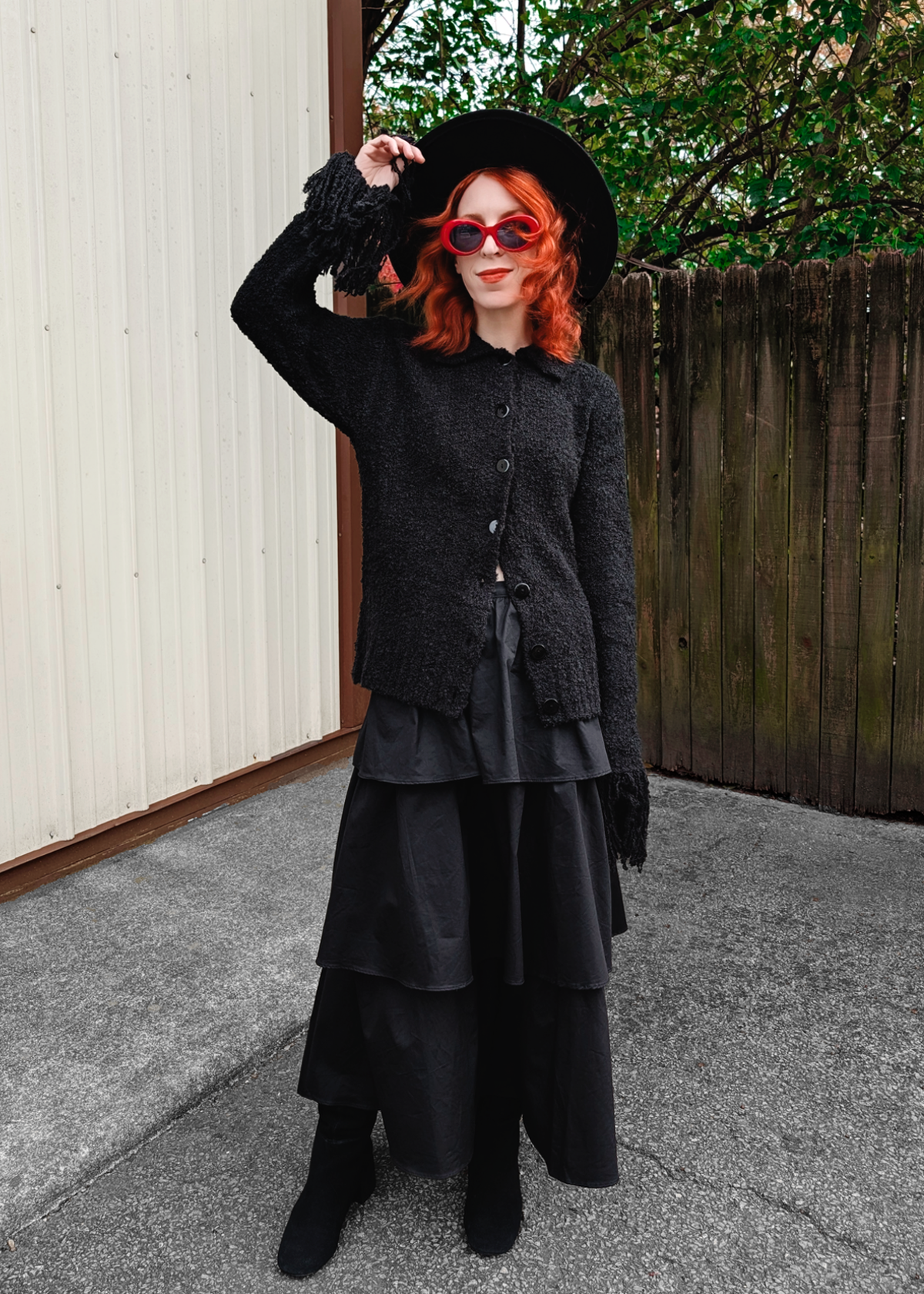 Person wearing a black cardigan and tiered ruffle skirt with a hat and sunglasses outdoors.