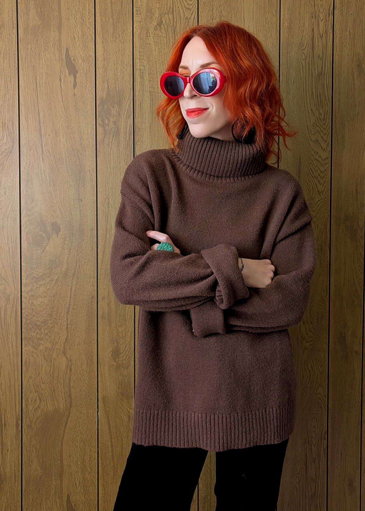 Woman wearing a brown sweater and sunglasses against a wooden wall
