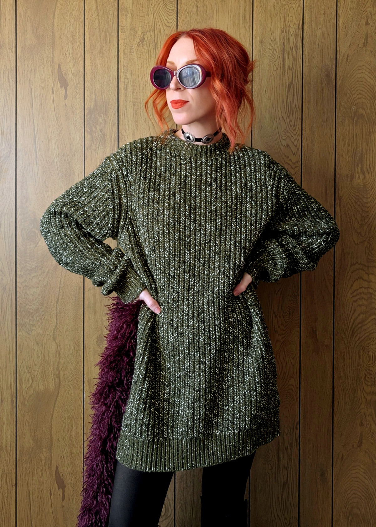 Person wearing a green knitted sweater against a wooden panel background
