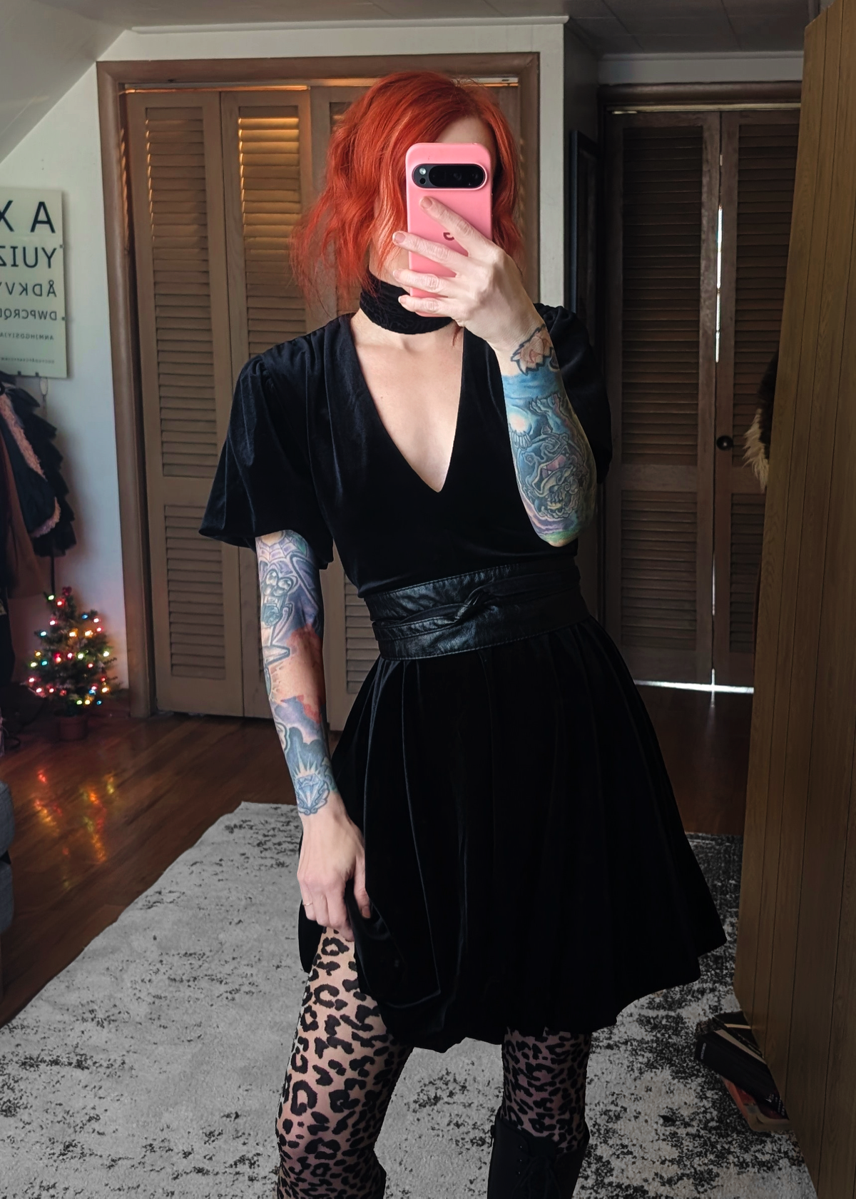Person wearing a black velvetdress with leopard print tights taking a mirror selfie.