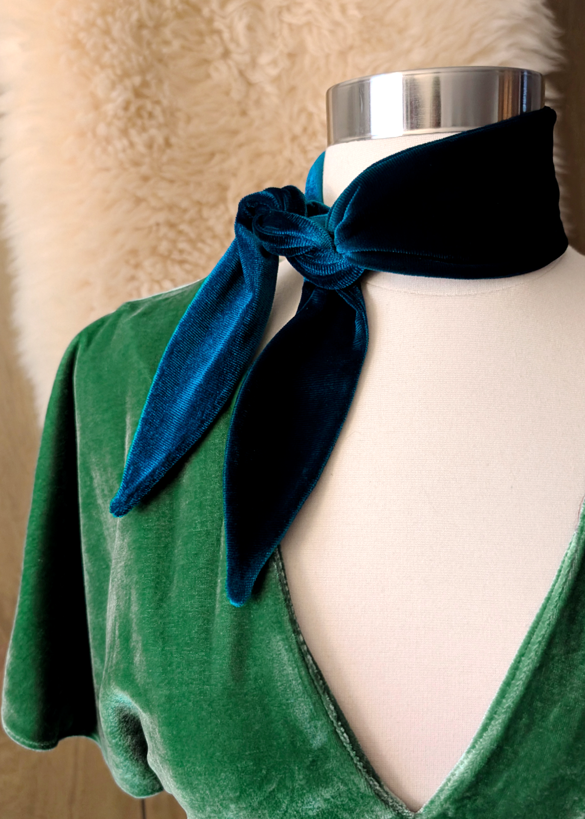 Mannequin wearing a green dress with a blue velvet scarf tied around its neck against a beige background