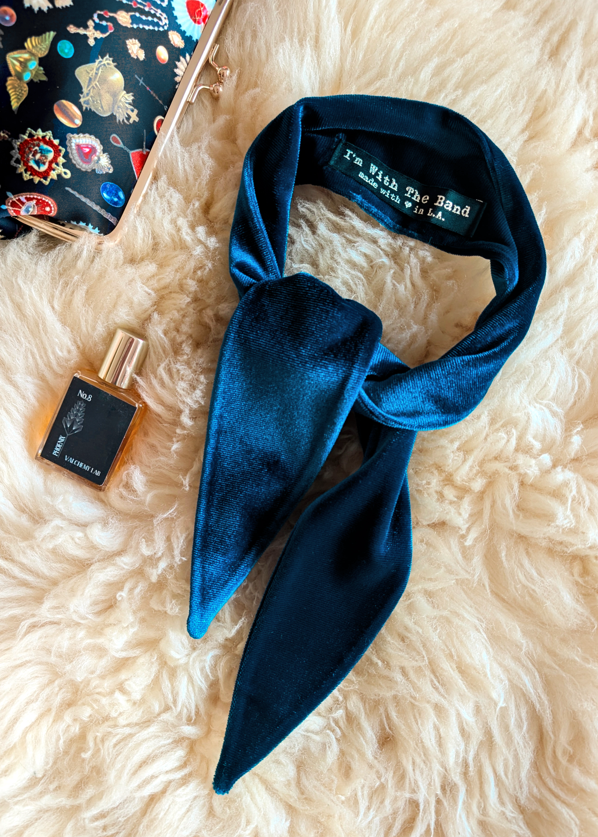 Blue velvet scarf and a small bottle of perfume on a fluffy white surface