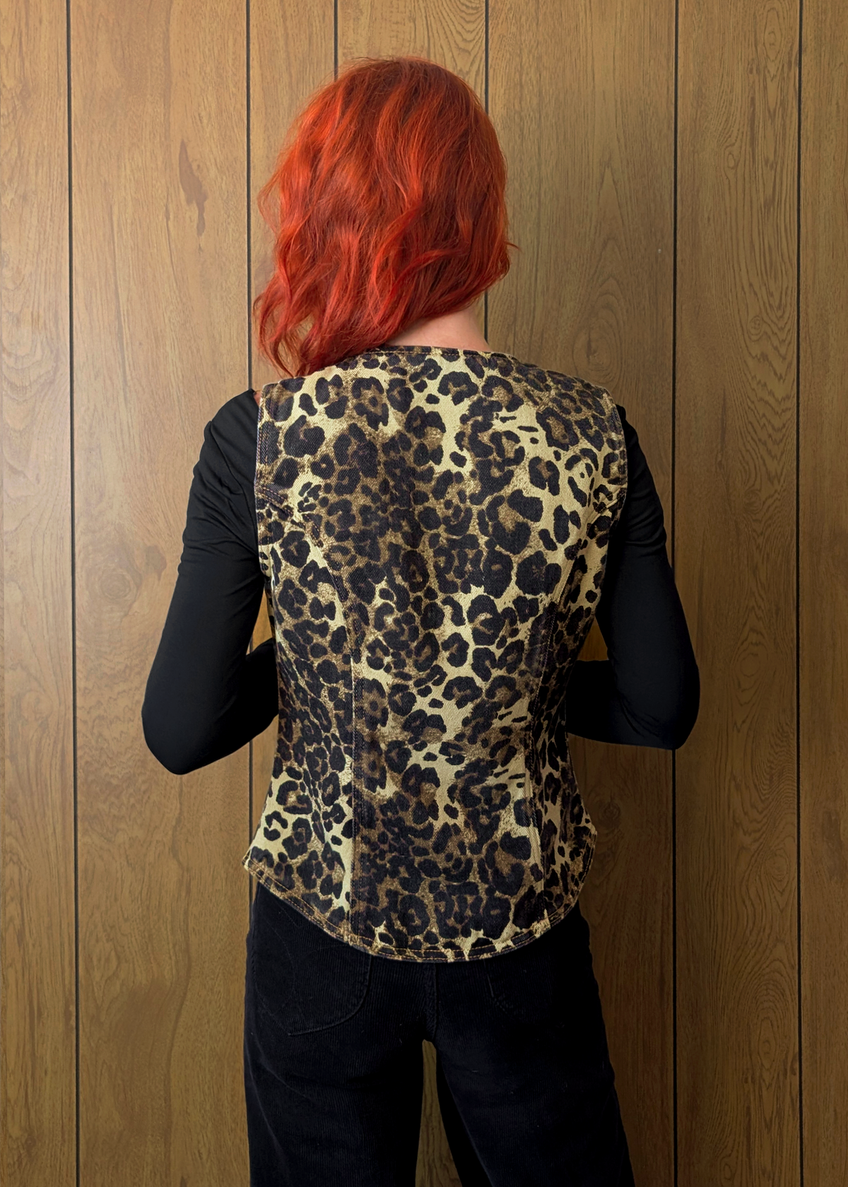 Person wearing a leopard print vest against a wooden wall