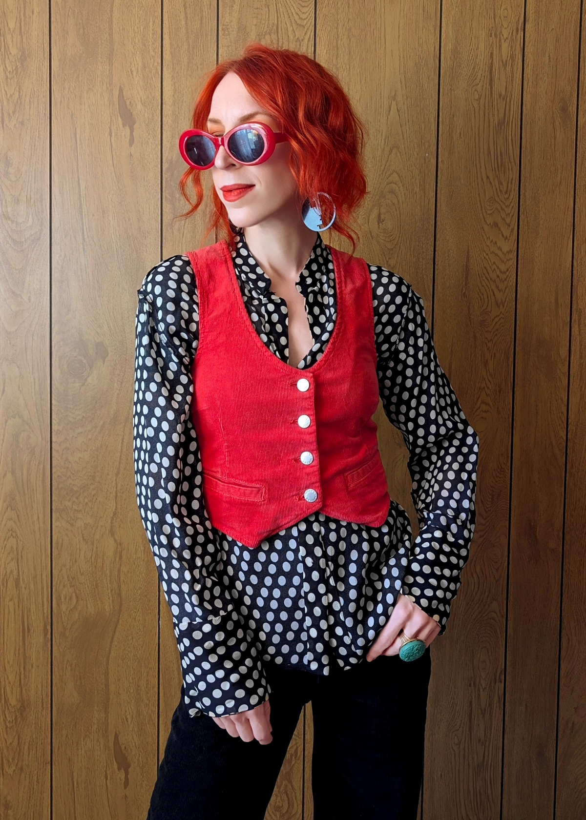 Person wearing a red vest over a polka dot shirt against a wooden background