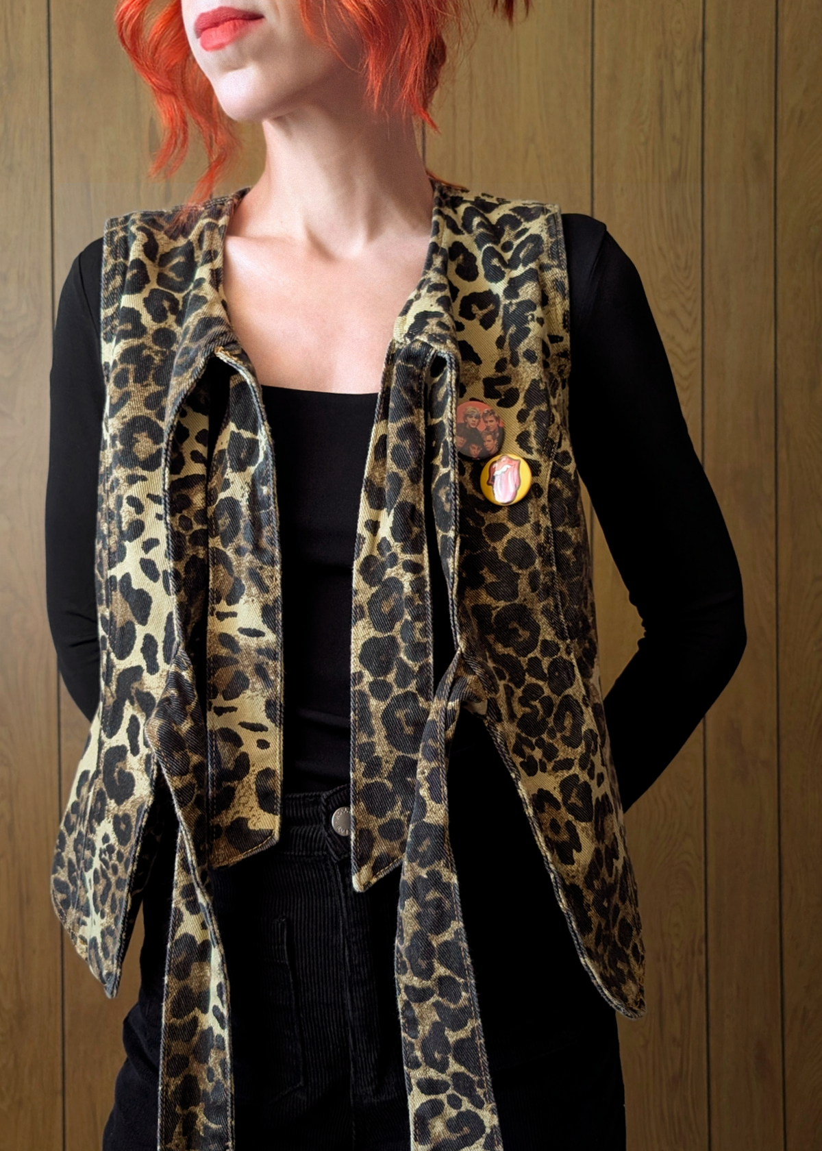 Person wearing a leopard print vest over a black top against a wooden background