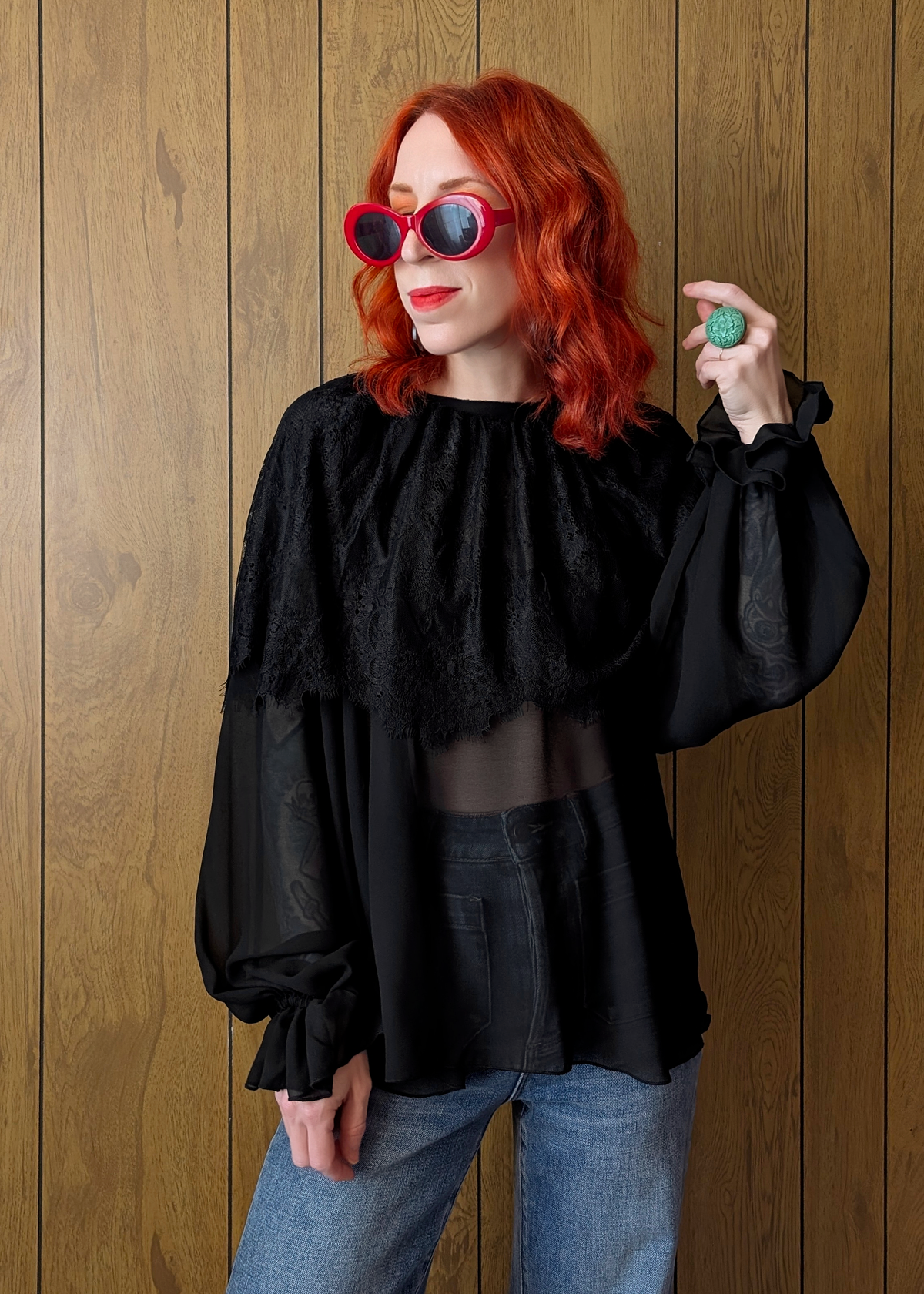 Person wearing a black lace chiffon blouse and blue jeans, against a wooden background