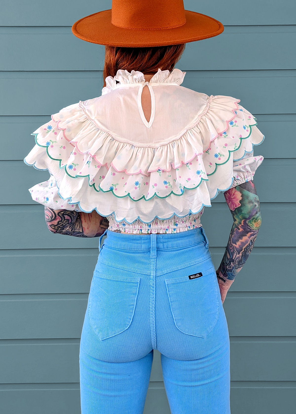 80s inspired prairie ruffle crop blouse with tiered ruffles, high neckline, embroidered floral details, puff sleeved, and smocked bottom. White cotton with blue and pink floral pattern. By Glamorous UK